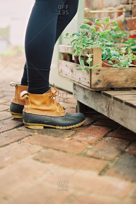 A woman wearing waterproof boots, with a box of seedlings.