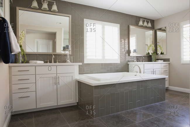 Spacious bathroom with tiled bath and white cabinets at home