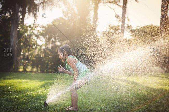 Girl standing in the spray of a water sprinkler