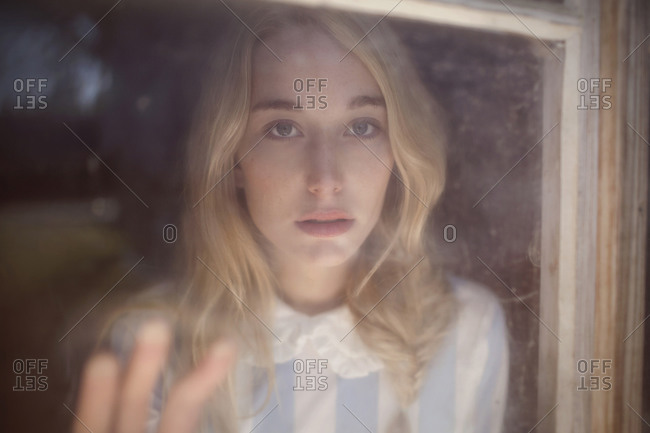 Blonde woman staring out of a dirty window