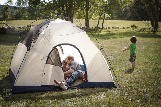 Two kids and a man hanging out in tent