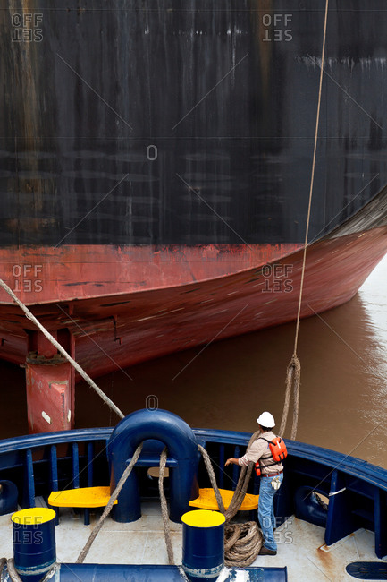 Tugboat crew member arranging cargo ship rope