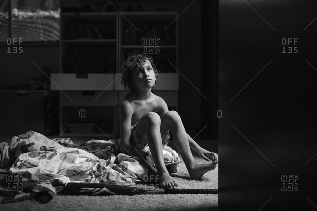 A boy sitting on a comforter on floor