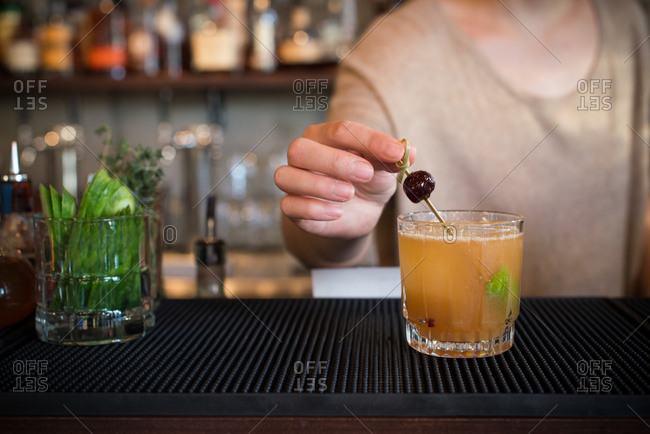 Female bartender garnishes cocktail with black olive