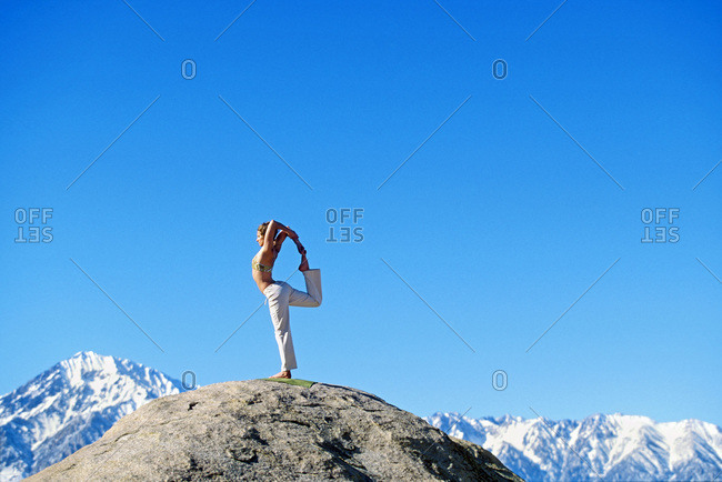 Woman displaying stength, balance, and focus in yoga pose on boulder in Buttermilk Country outside of Bishop, California with Mt.