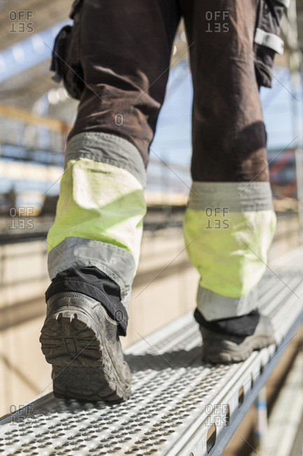 Low section rear view of worker walking on metal platform at construction site
