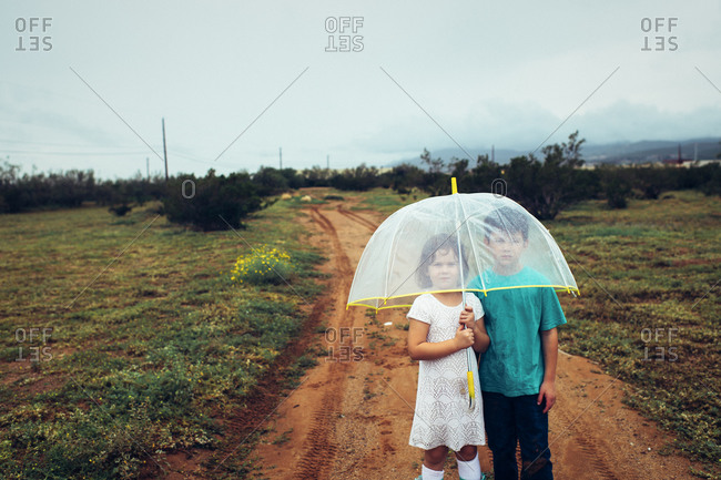 Girl and boy under clear umbrella on dirt path