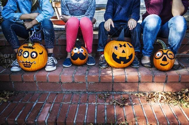 Children sitting on a porch with decorated pumpkins on Halloween