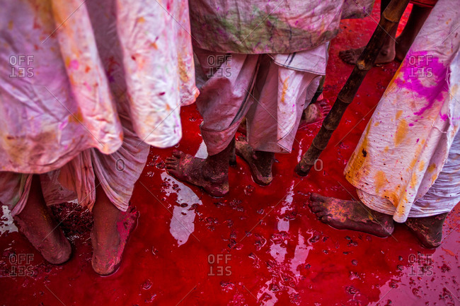 Men standing in red paint puddle at the festival of Nandgaon Holi in Mathura, India
