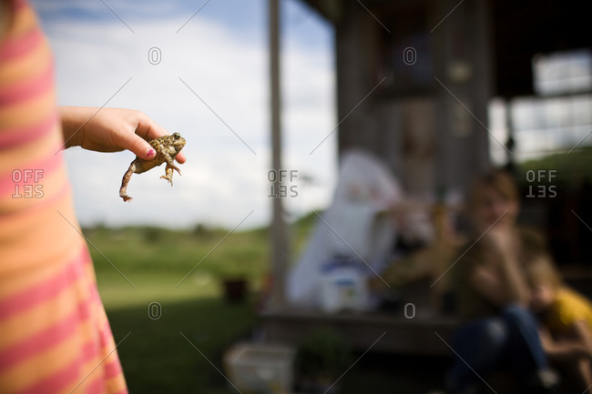 Girl holding a frog near rural house