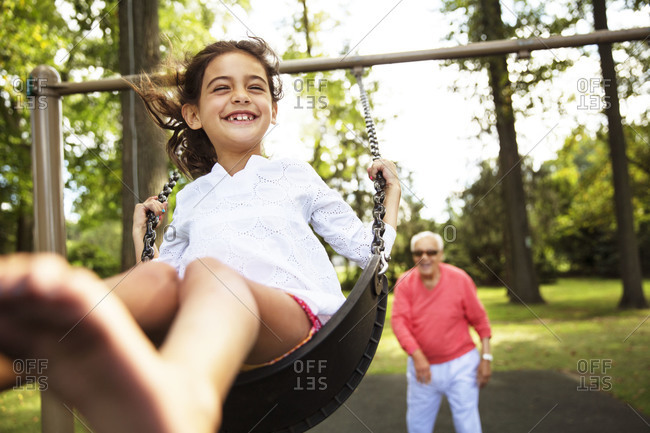 A grandfather pushes his granddaughter on the swing