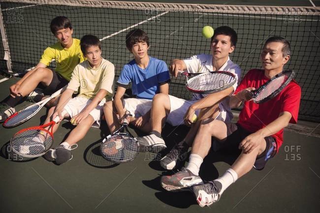 Boys and man resting at tennis net