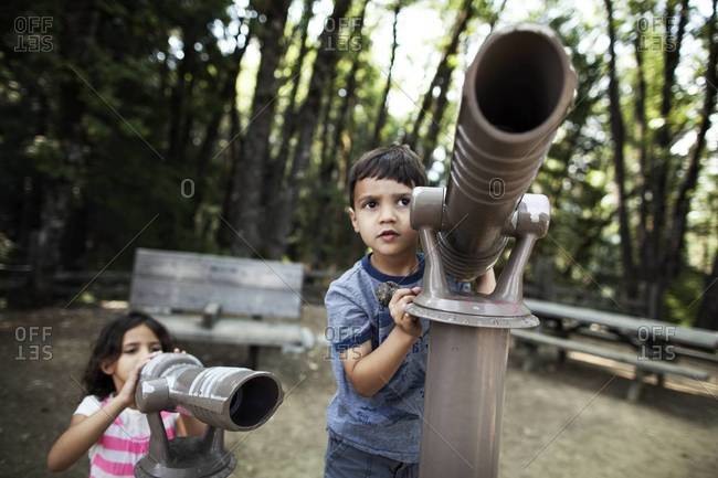 Children standing by telescopes in a forest