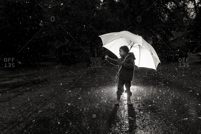 Boy playing in rain at night with umbrella