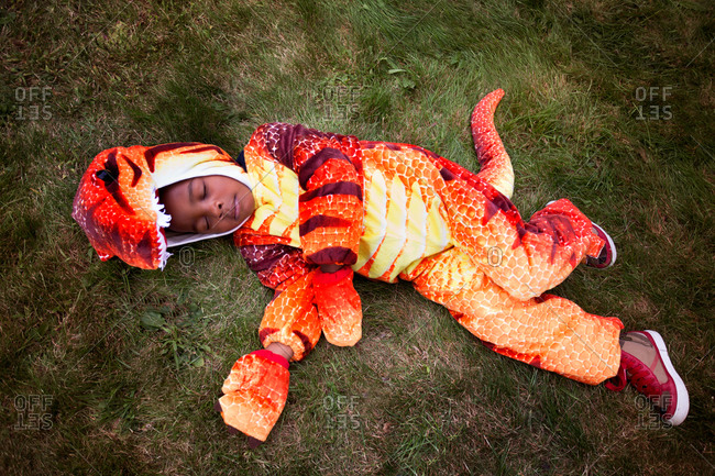 Boy in dinosaur costume laying on ground