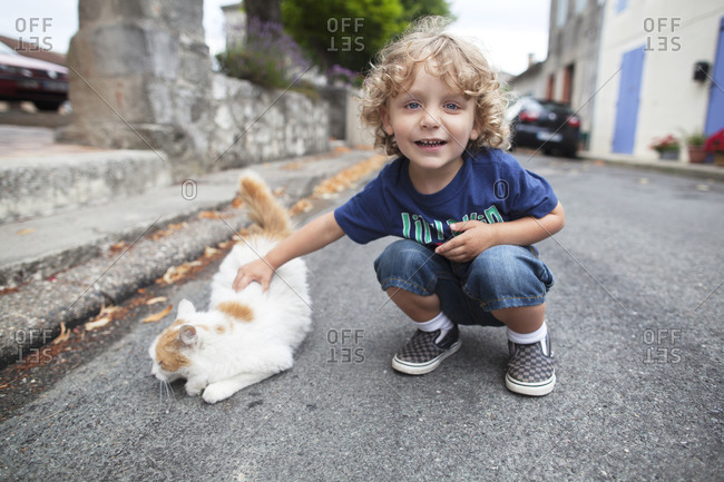 Young boy patting a cat on a street