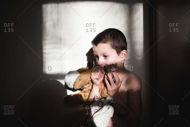 Young boy sucking his thumb while hugging his stuffed toys