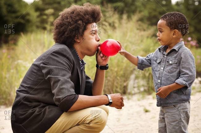 Young man blowing balloon for boy on shore