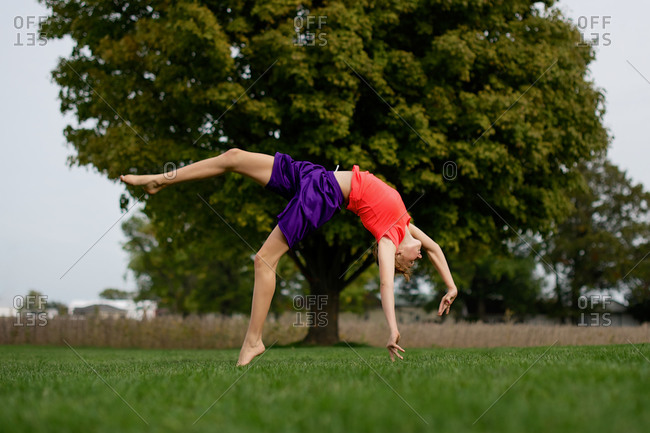 A girl does a back flip in a field