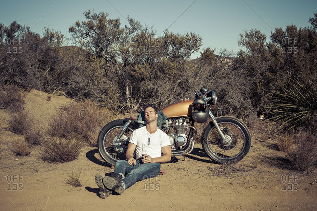 Man leaning against his motorcycle in the desert