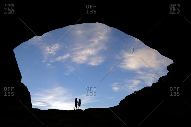Two young boys stand under a rock arch