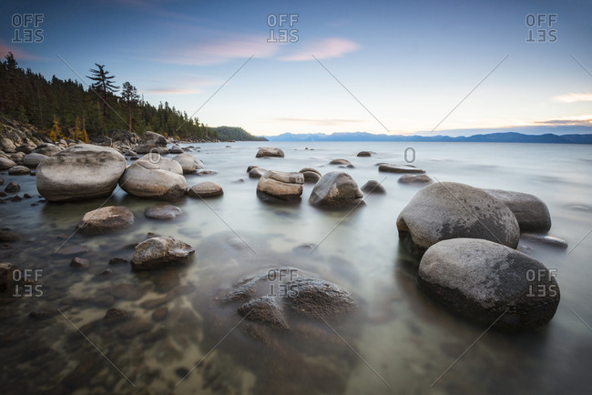 Sunset over calm water and granite boulders on the east shore of Lake Tahoe, Nevada
