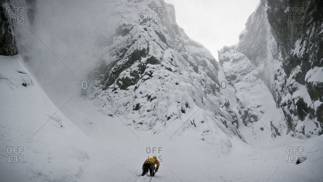An ice climber wading through deep snow to access a frozen gully in a Norwegian fjord