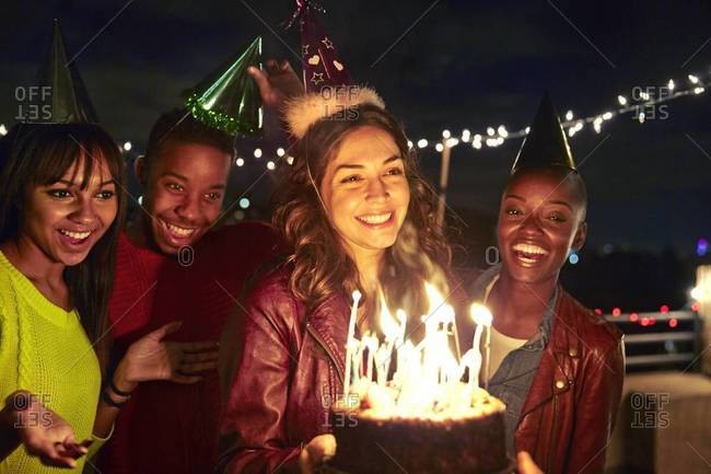 Hispanic woman holds birthday cake surrounded by friends