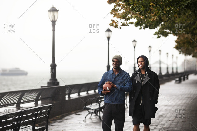 Two men walk along the waterfront holding a football