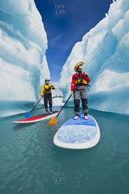 A couple on SUP board explore an iceberg canyon on Bear Lake in Kenai Fjords National Park, Alaska