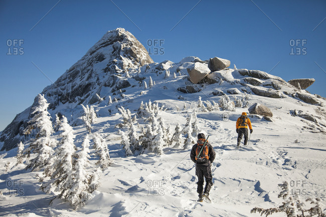 Two climbers wearing backpacks walk a snow-covered ridge in the Coquihalla Recreation Area of British Columbia, Canada