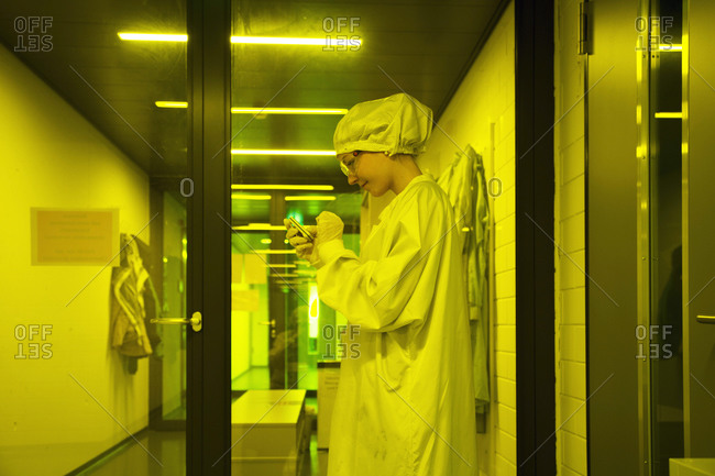 Female technician working in optical clean room unit, using mobile phone