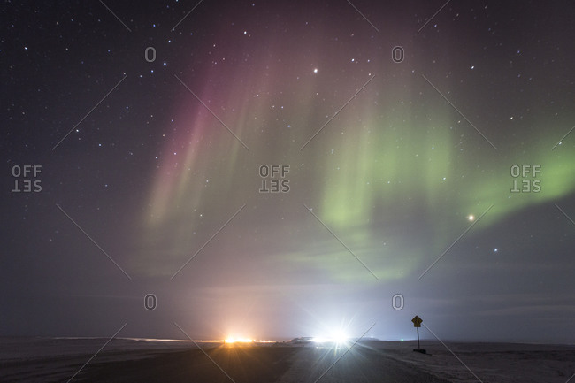 Shimmering pink and green Northern lights over distant town