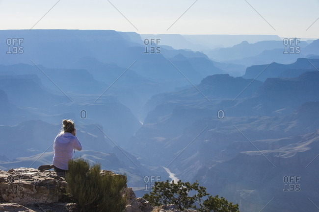 Woman sitting on the cliff of the desert view point over the Grand Canyon, Arizona