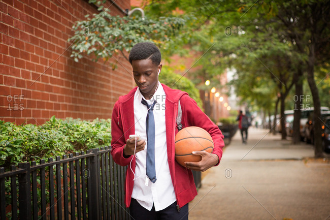 Teenage boy walking on a street with a basketball and a smartphone