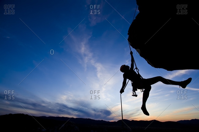 Silhouette of climber hanging from a challenging cliff