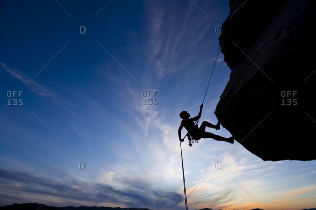 Silhouette of person climbing up a cliff