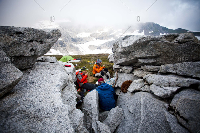Three climbers eat dehydrated food between rocks hoping to avoid the wet conditions