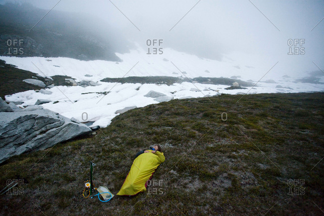 A climber sleeps outside in a bivy sack underneath a cloudy sky