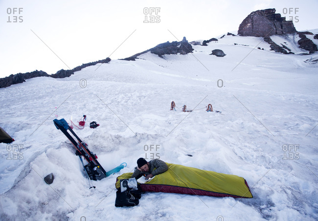 A young climber lies in his bivy sack and reads a book while the sun sets at base camp on Mount Rainier