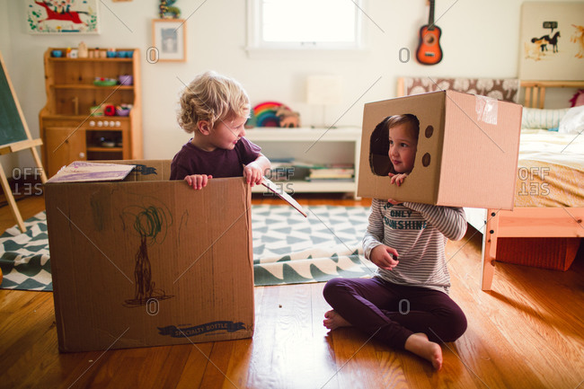 A brother and sister play with cardboard boxes