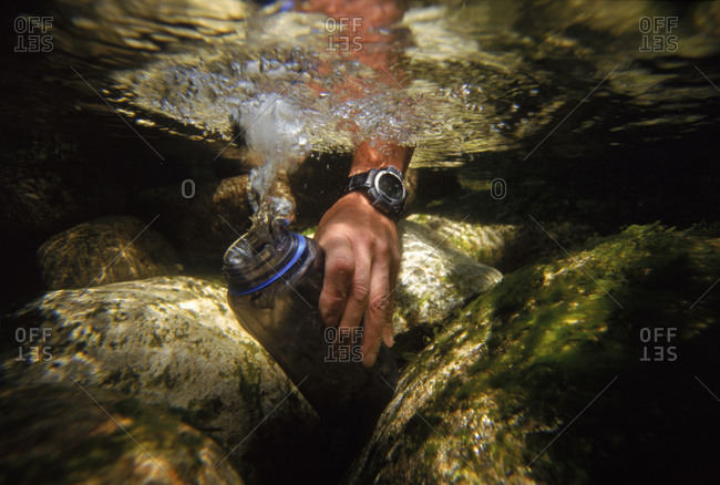 Underwater of person filling water bottle in stream