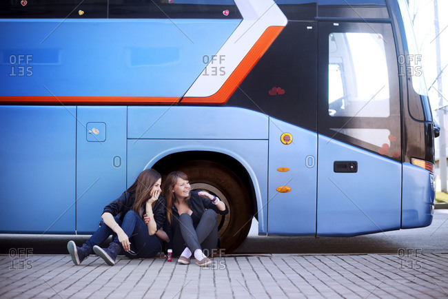 Two teen girls sitting in front of tour bus