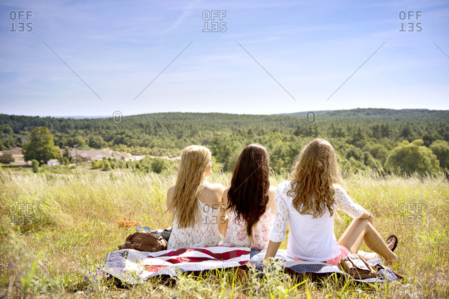 Three friends sit on a picnic blanket