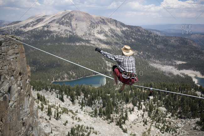 Male highliner in cowboy hat stands up on a 125 foot highline over a lake in a gap on top of Mammoth Crest