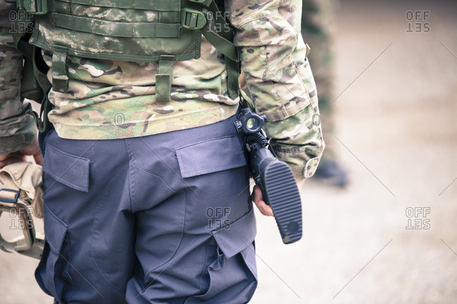 A man in camo gear carries a gun and goggles