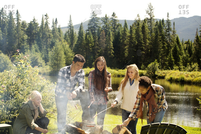 Teens roasting hot dogs over a campfire by lake