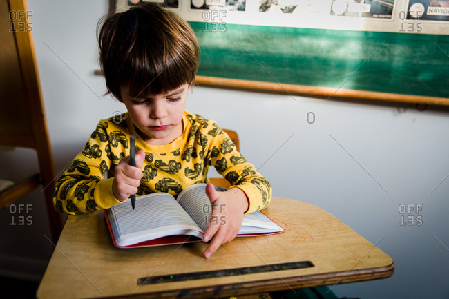 A boy sits at a school desk and doodles