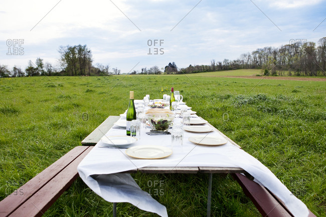 A picnic table set with linens and china in the middle of a field