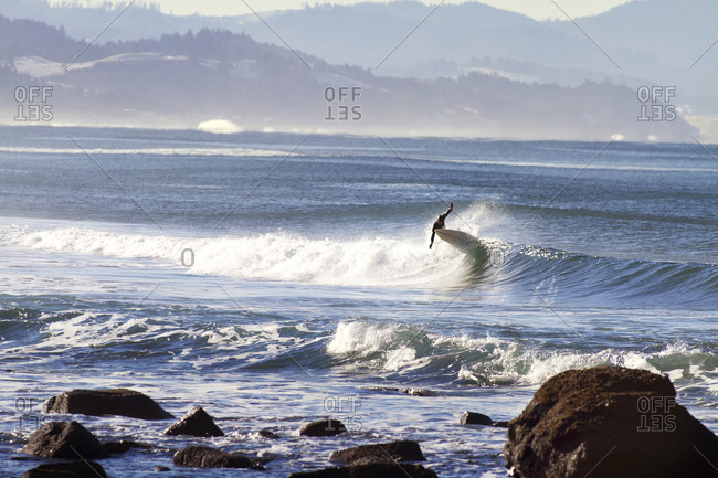 Surfer riding waves off a rocky coastline